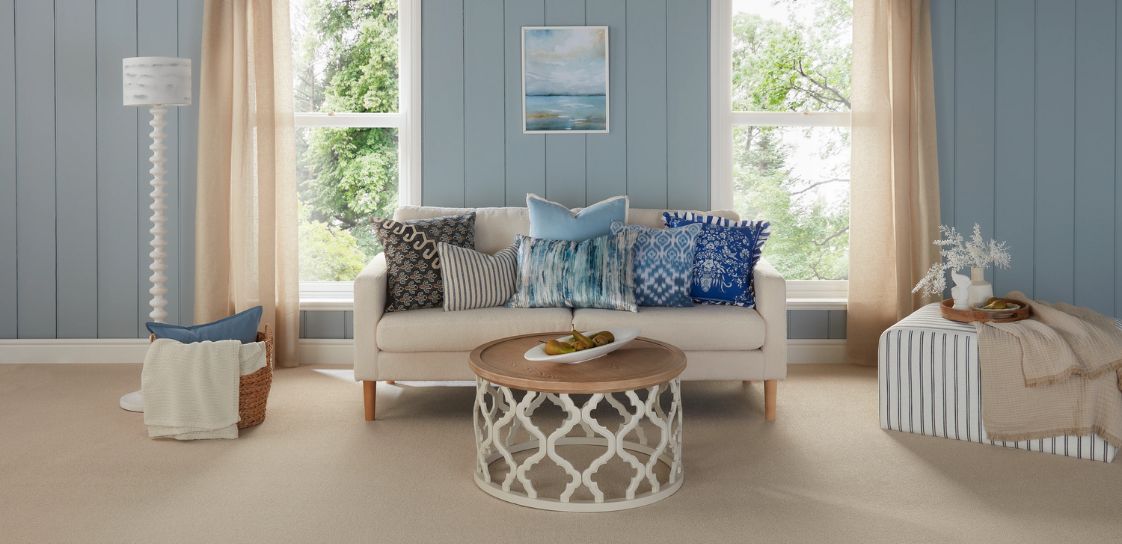 A living room with nuetral carpet and furniture, dressed with pale blue accessories and panelling.